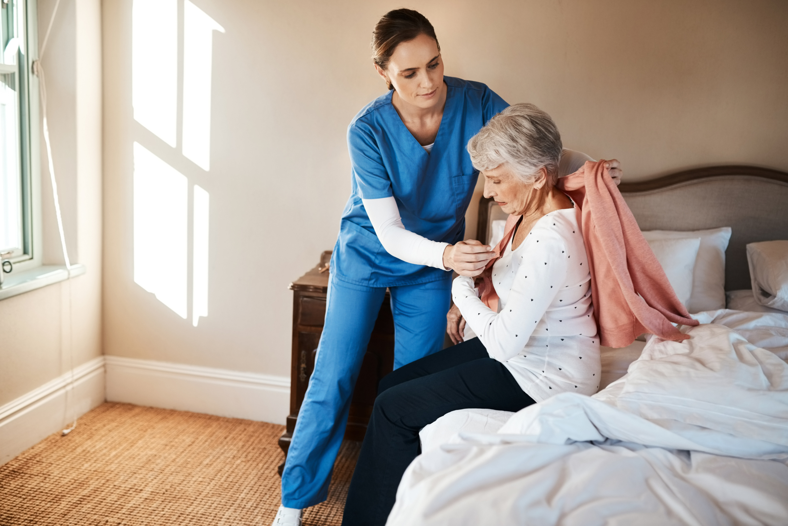 Caregiver helping patient get dressed and assisting with getting out of bed.