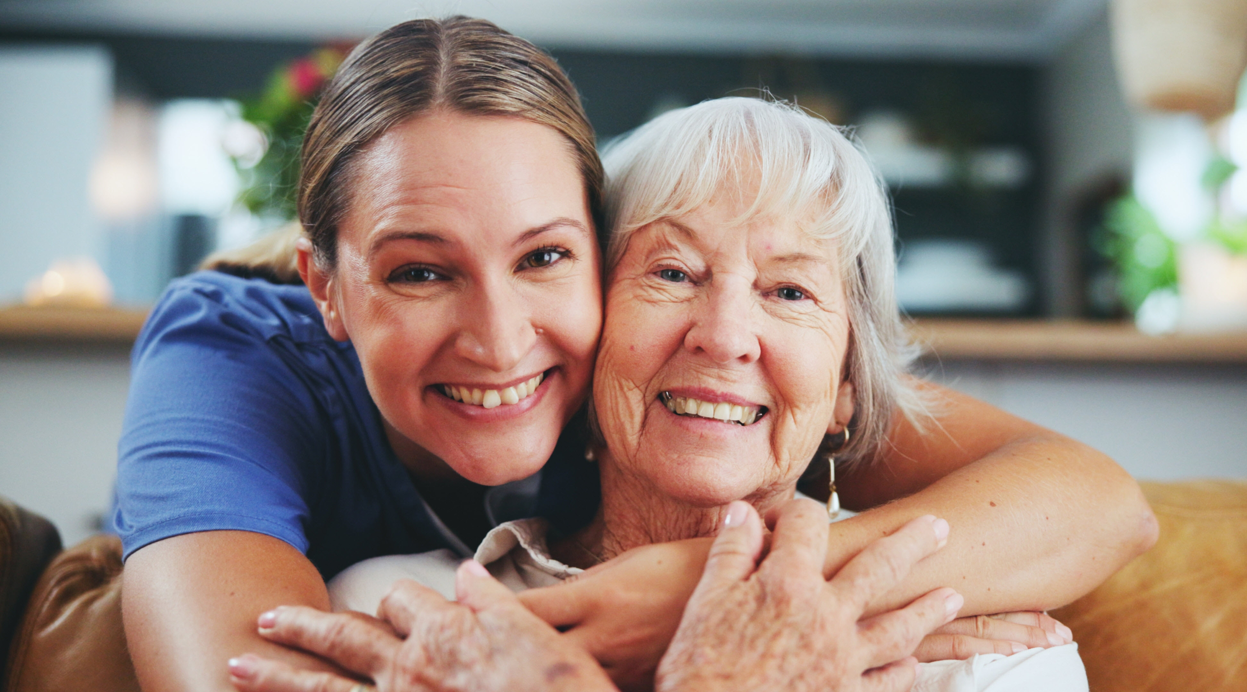 An adult daughter smiling and hugging her happy senior mother.