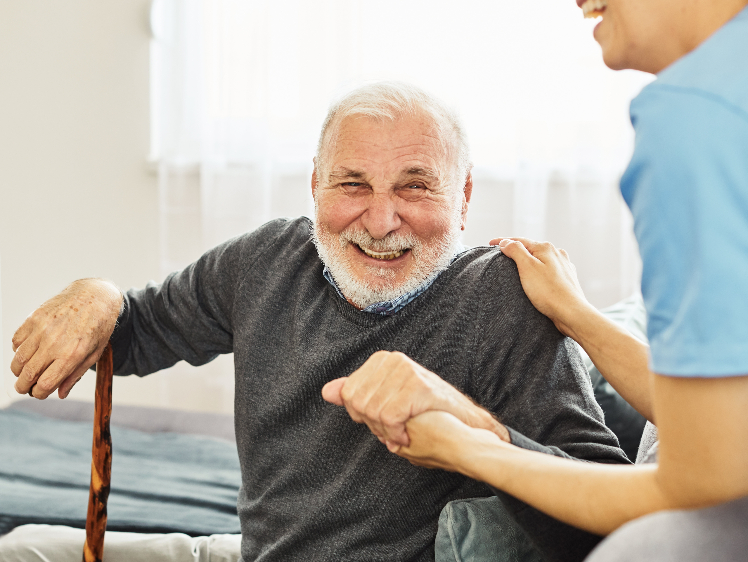 A senior man smiling and laughing as he recovers at home after a hospital stay with the help of a caregiver.